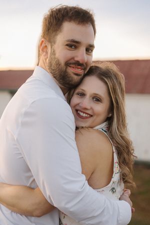 A romantic couple embraces and laughs together during a sunset photoshoot outdoors.