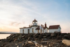 West Point Lighthouse stands majestically on rocky shores against a pastel sunset sky in Seattle, Washington.