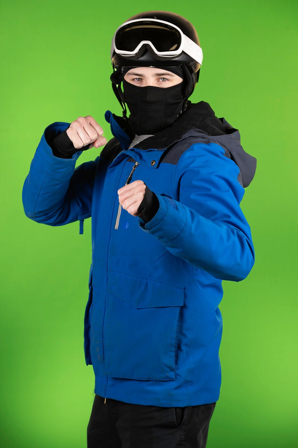 Person in blue ski jacket and goggles poses against bright green screen background.