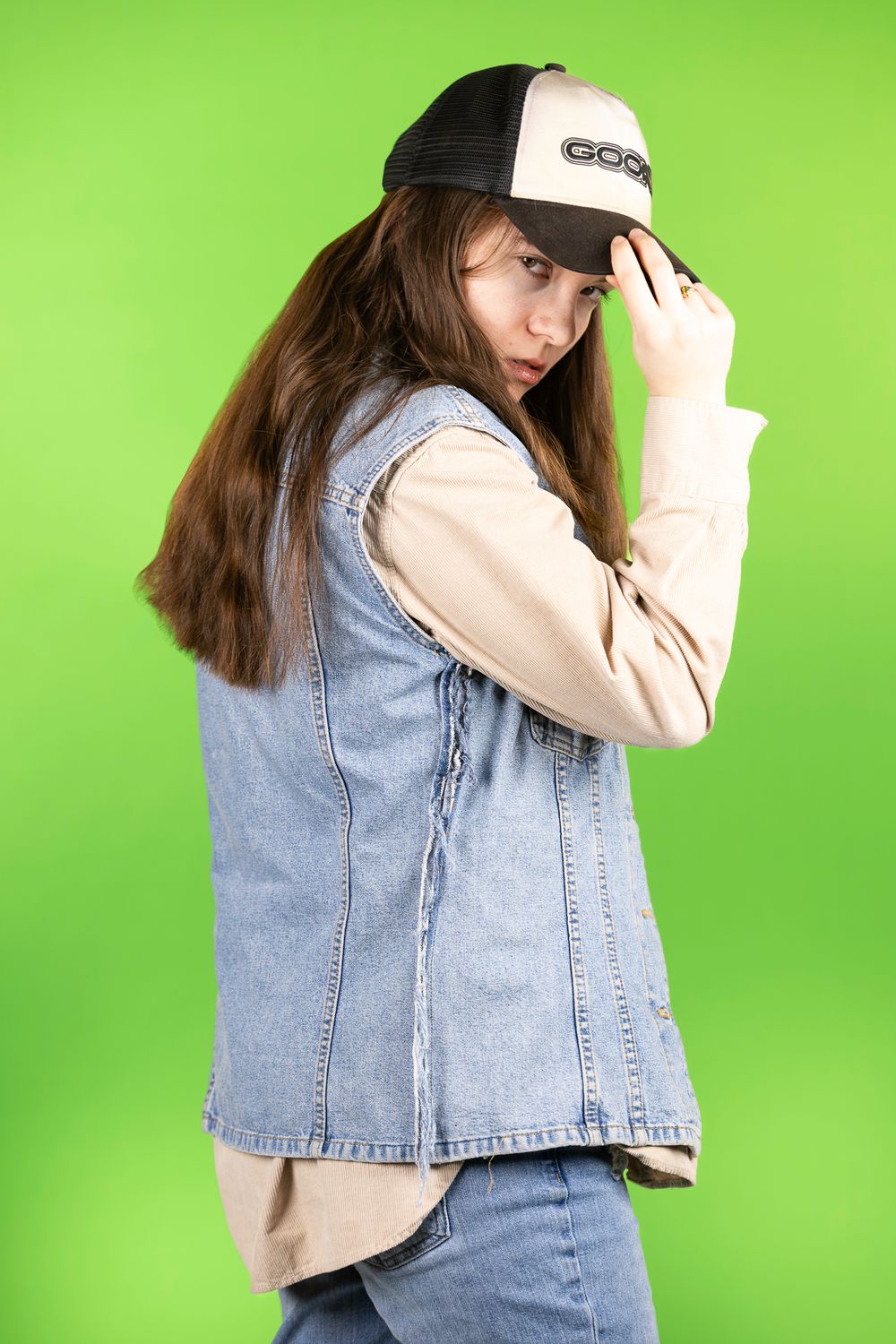 Person wearing denim vest and beige sweater poses against bright green background.