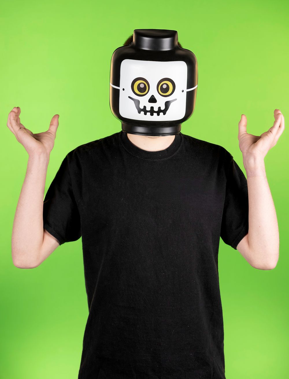 Person in black shirt wearing cartoon-style mask poses expressively on green background.