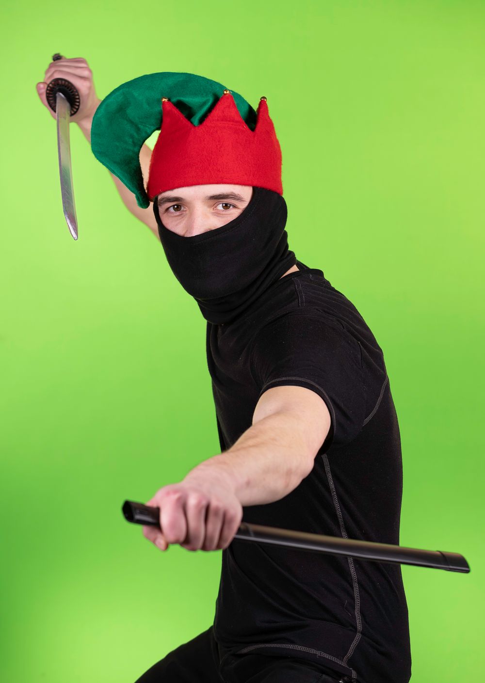 Figure in ninja costume with red elf hat demonstrates martial arts moves against green screen.