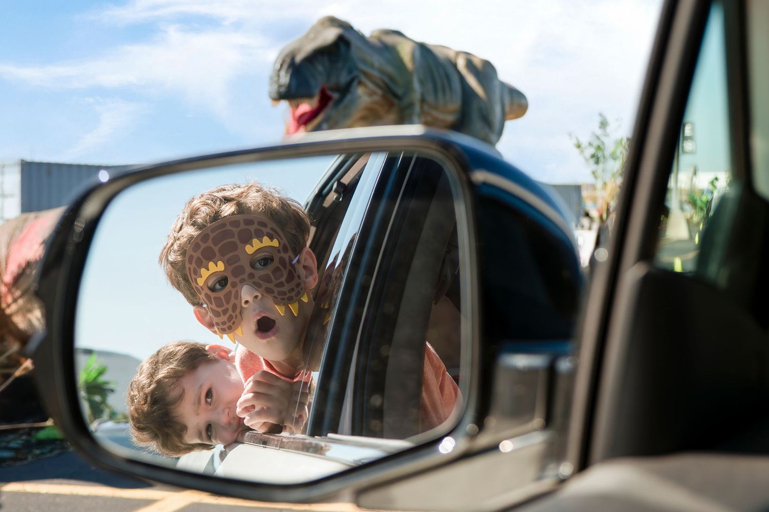 Two children's faces reflected in a car side mirror with playful expressions.