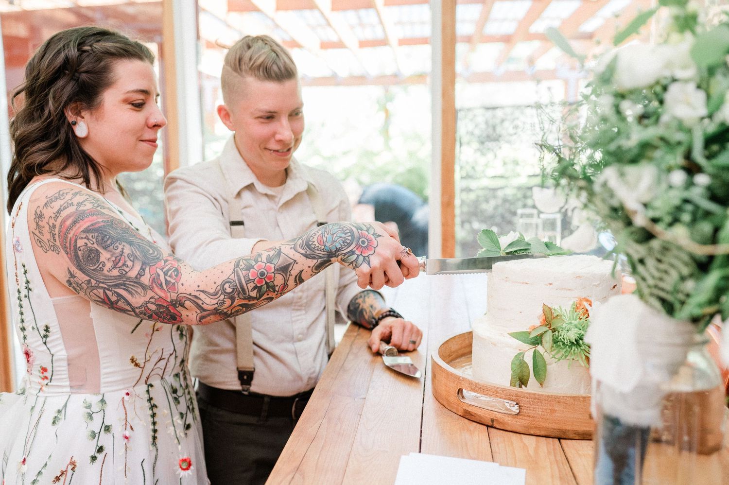 Two brides cutting their wedding cake together during their wedding