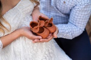 Close-up of expectant couple holding small brown leather baby shoes in their hands outdoors.