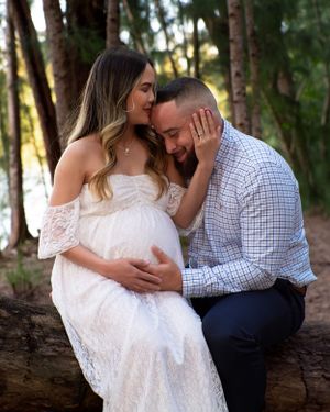 Man tenderly kissing pregnant woman's cheek as she cradles his face during forest maternity session.