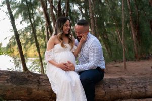 Couple sharing a joyful maternity photo session sitting on a log in a forest near a lake.