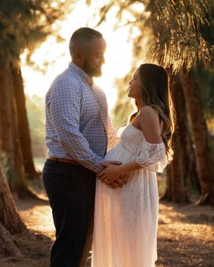Expectant couple holding hands and gazing at each other during a golden hour maternity photoshoot.