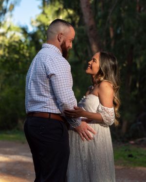 Expecting couple sharing a joyful moment together on a sunlit path during outdoor maternity session.