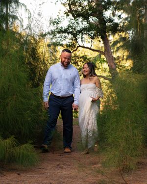 Couple walking hand in hand through lush green forest path during golden hour maternity photoshoot.