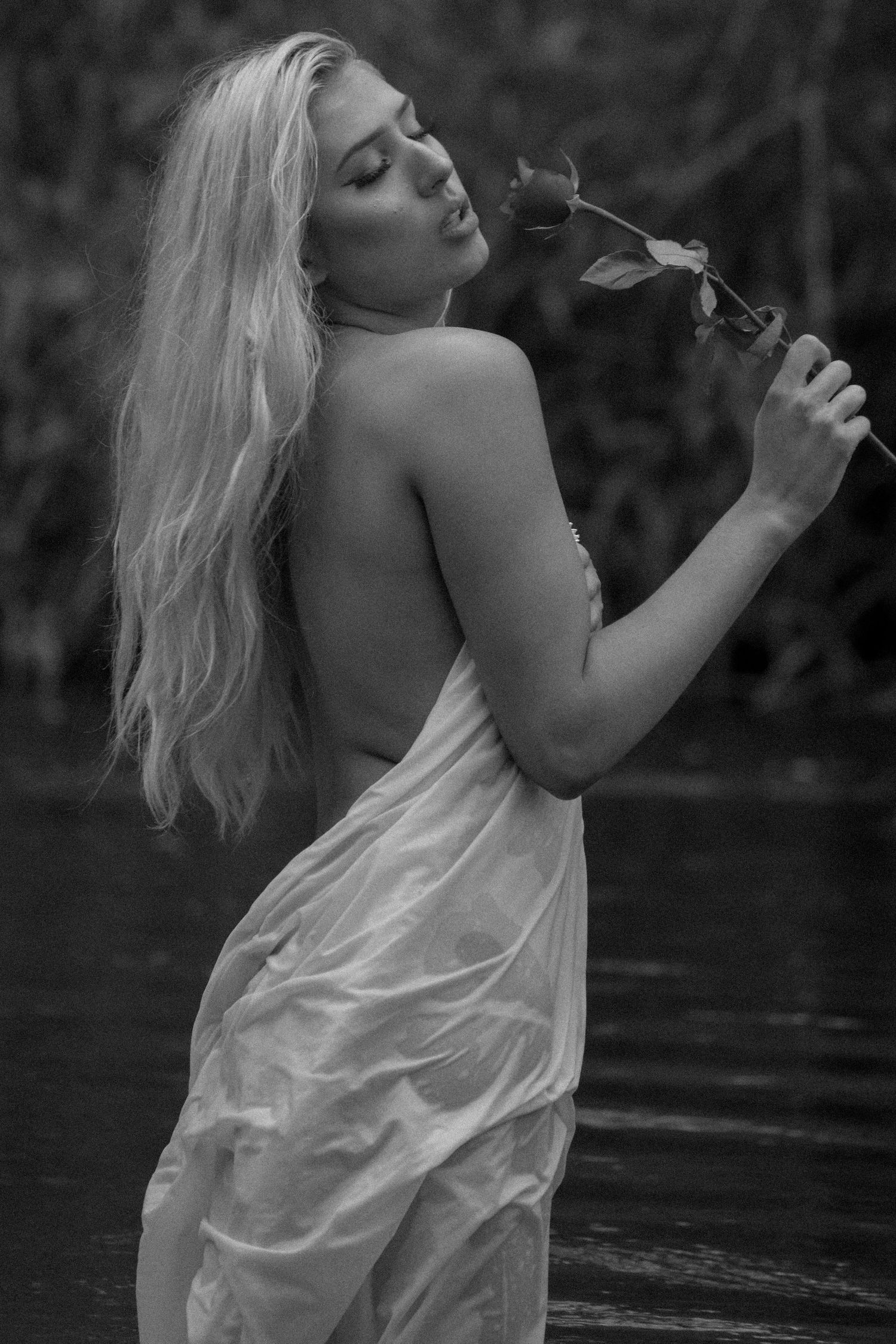 Black and white photo of blonde woman holding a rose while standing in water.