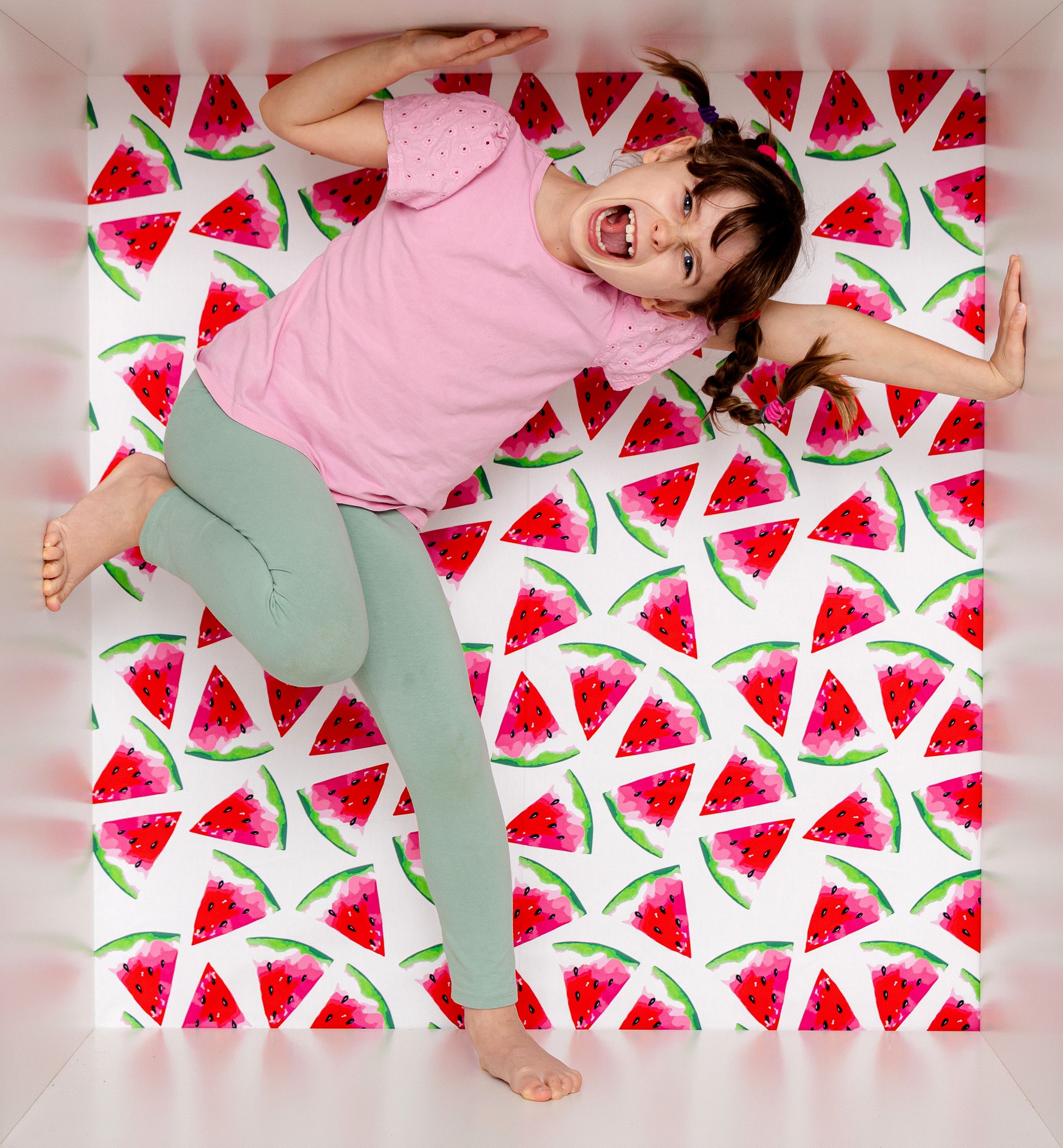 Person in pink shirt laying on watermelon print blanket with mint green pants makes playful poses.