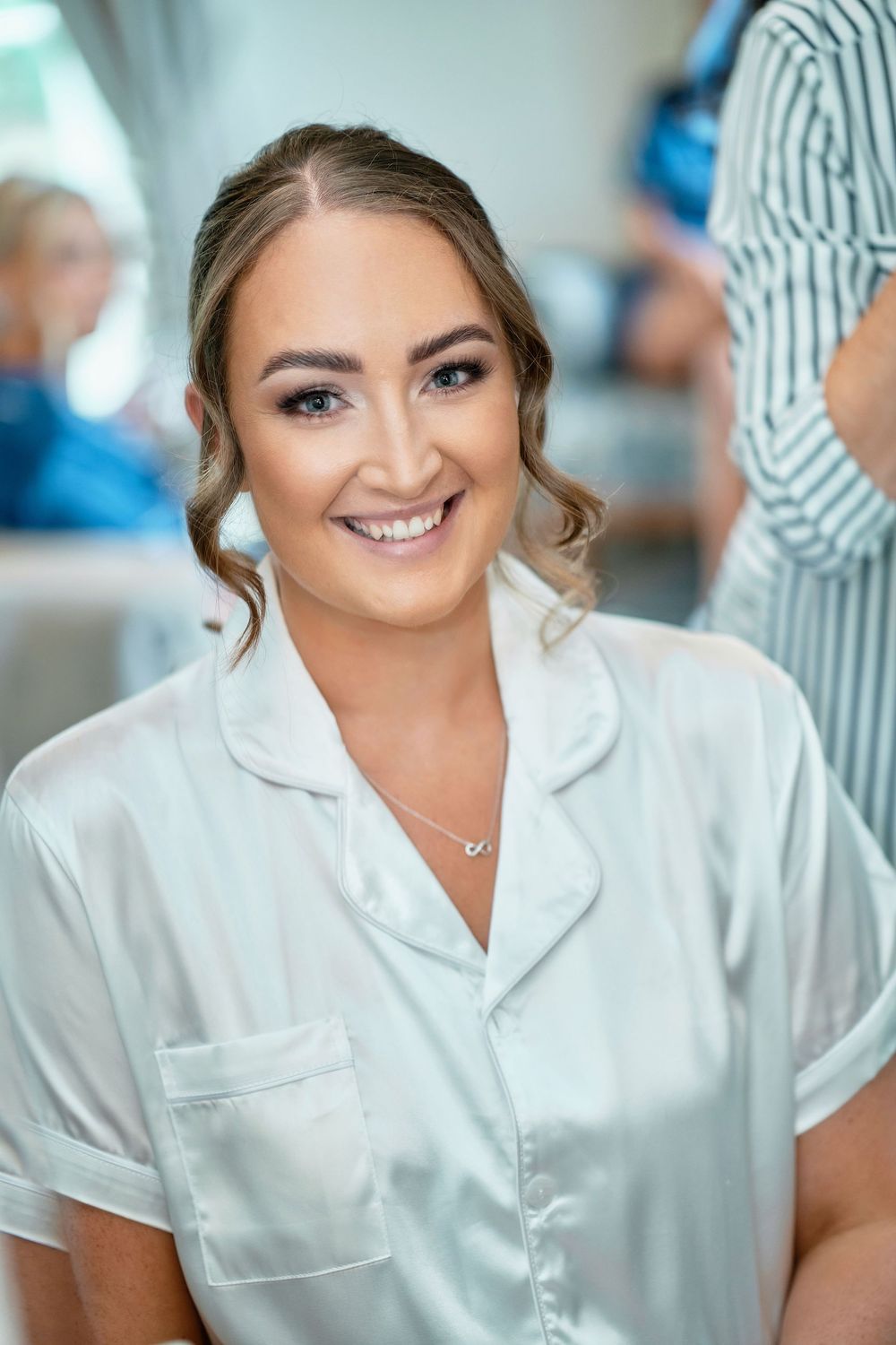 A healthcare professional in a white uniform smiles warmly in a medical setting with soft blue lighting in the background.