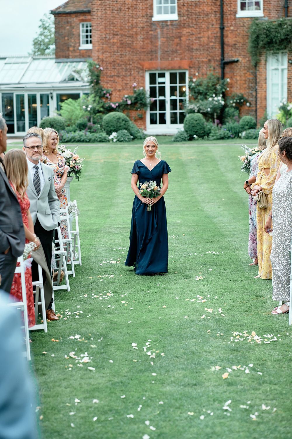 Outdoor garden wedding ceremony with guest seating on lawn and historic brick house in background.