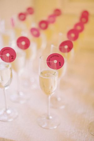 Champagne glasses adorned with numbered pink circular tags sit in a row on a white tablecloth.