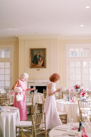 Elegant white reception hall set with round tables, gold chiavari chairs, and pink floral centerpieces for an upscale event.