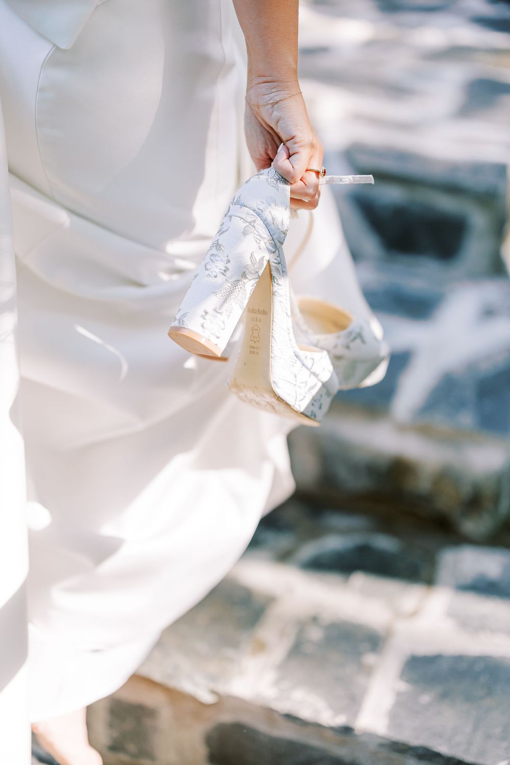 A sparkly silver wedding shoe peeks out from beneath a flowing white dress on stone steps.