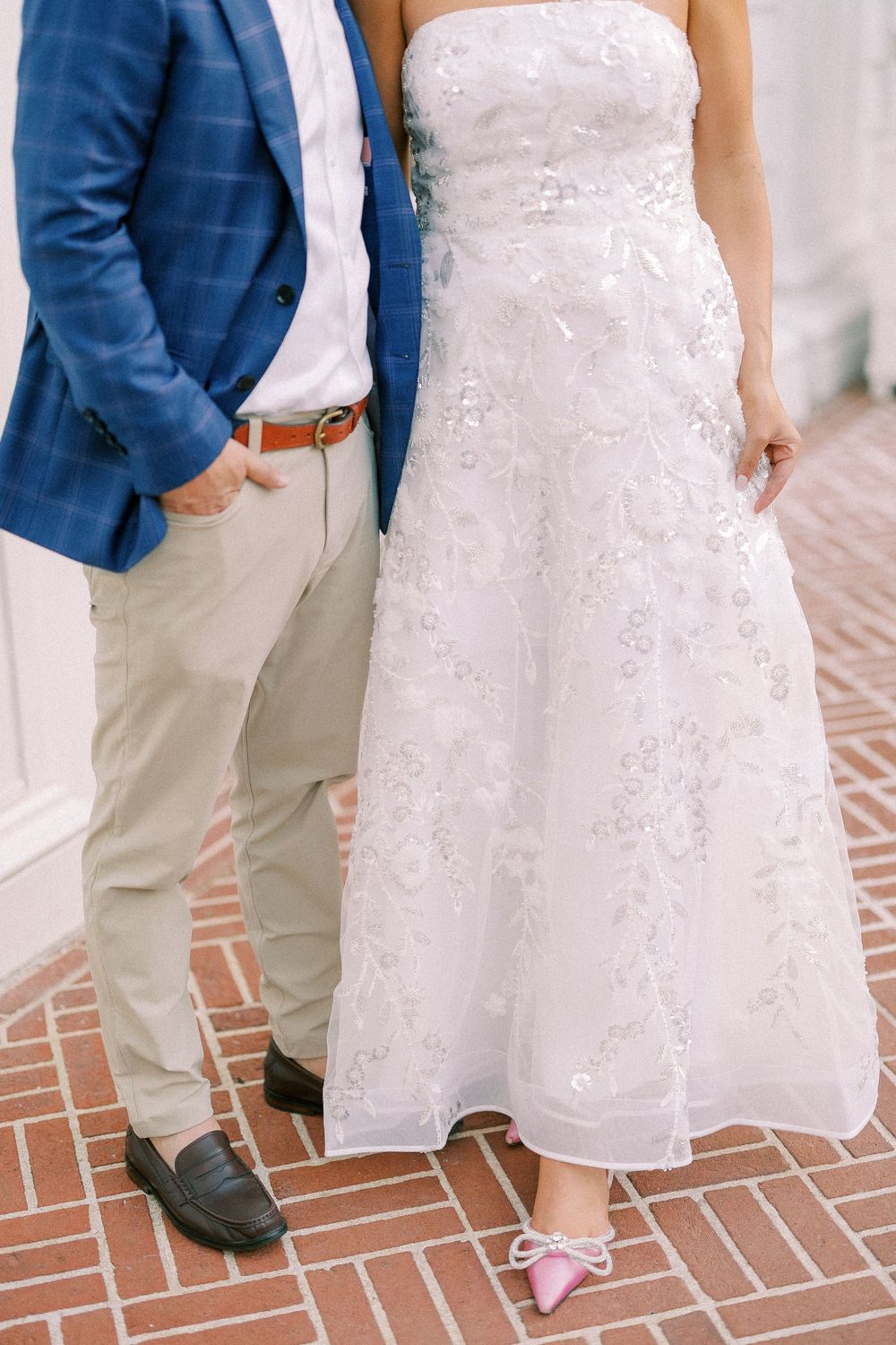 Close-up view of wedding attire showing a blue blazer, khaki pants, and bridal gown against a brick pathway.