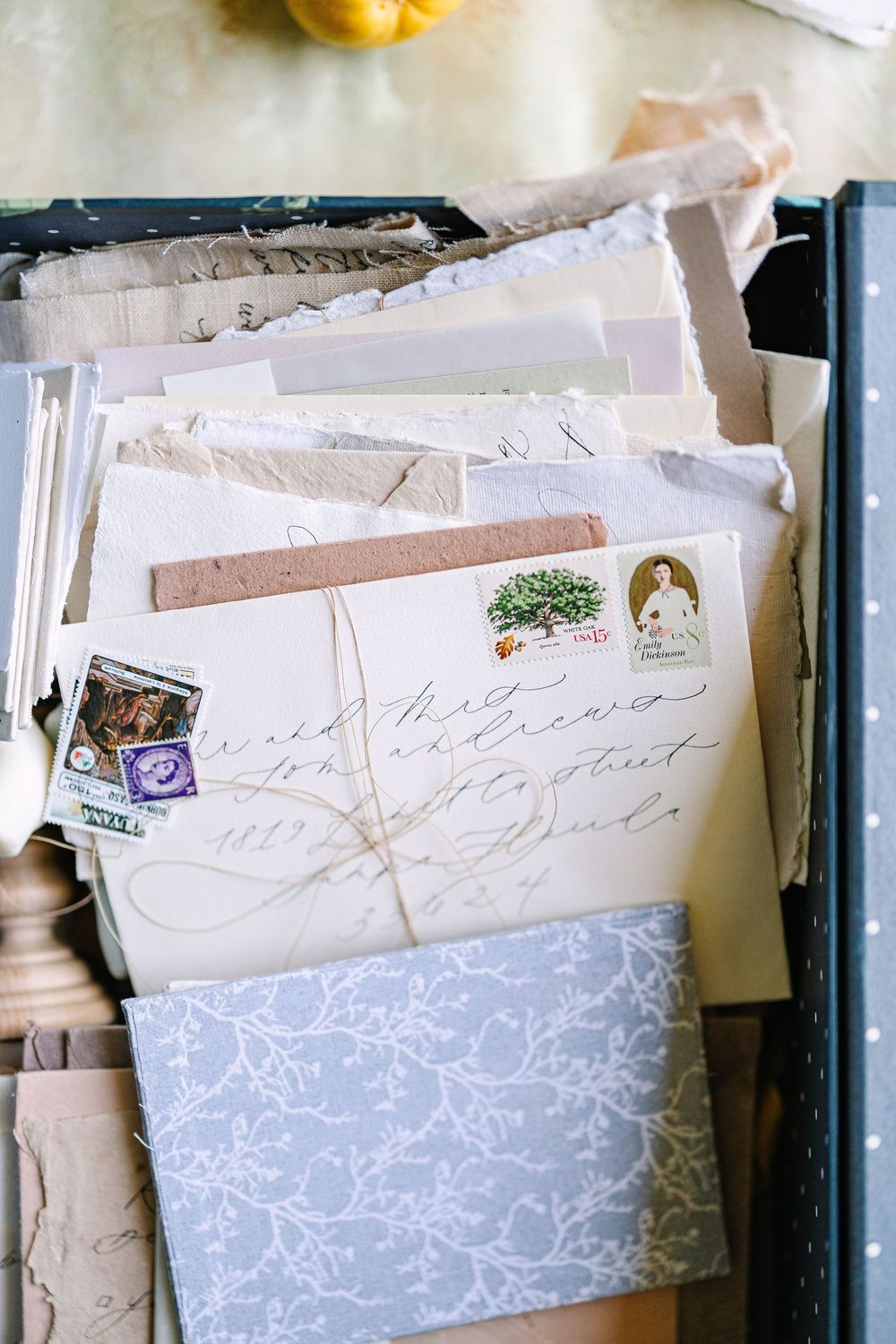 Stack of vintage letters and envelopes with postage stamps and decorative floral pattern paper in soft blue tones.