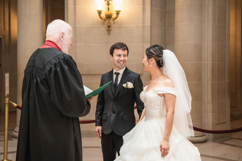 A joyous wedding ceremony takes place indoors with the couple and officiant sharing a lighthearted moment at the altar.