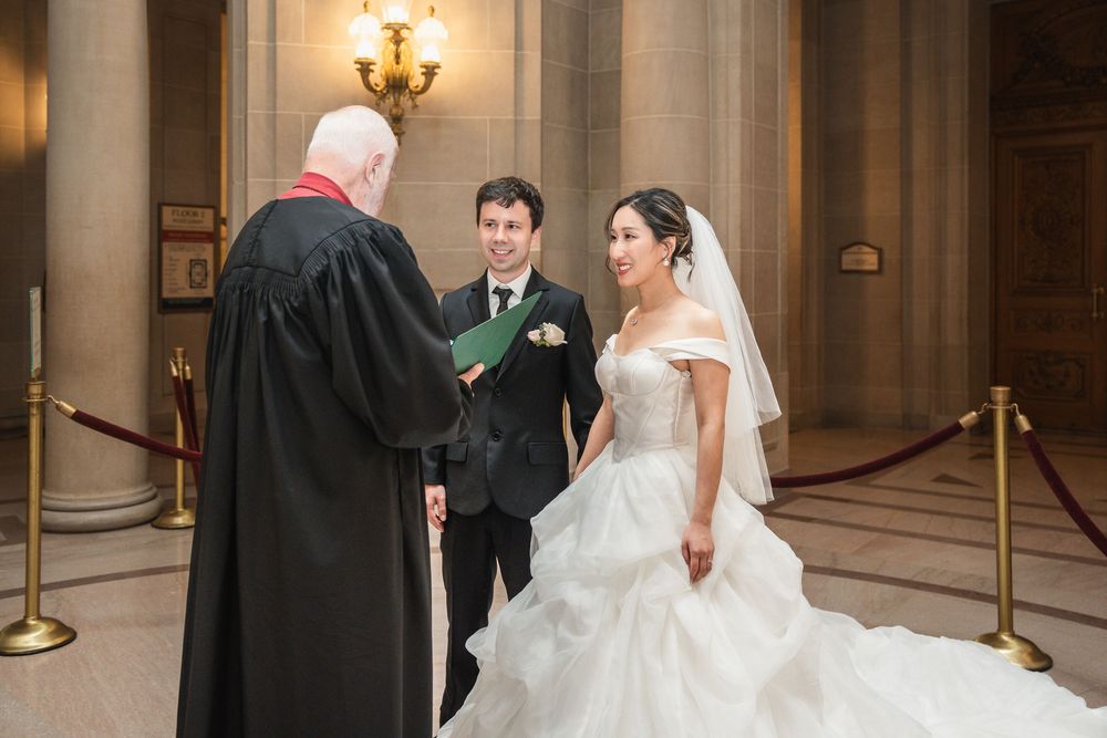 A couple shares a romantic moment in the stately halls of a grand City Hall during their wedding ceremony.