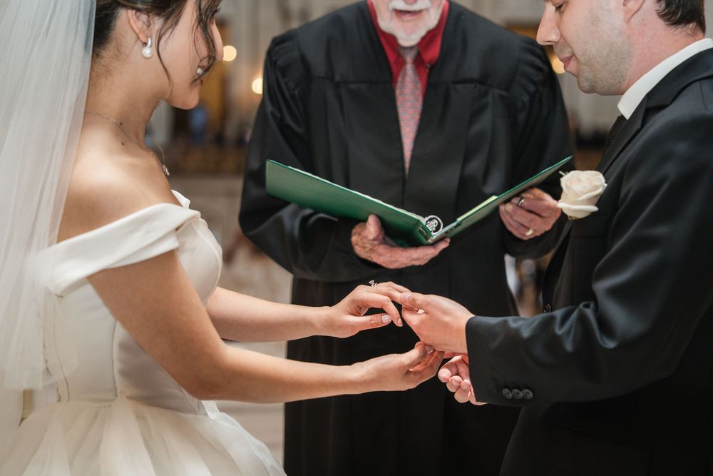 Hands exchanging rings during a traditional wedding ceremony at an elegant indoor venue where vows are being exchanged.
