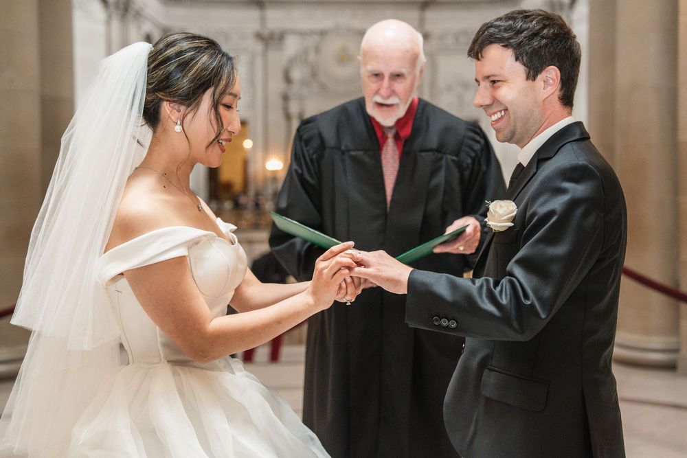 Intimate wedding ceremony exchange in a grand marble corridor with vaulted ceilings.