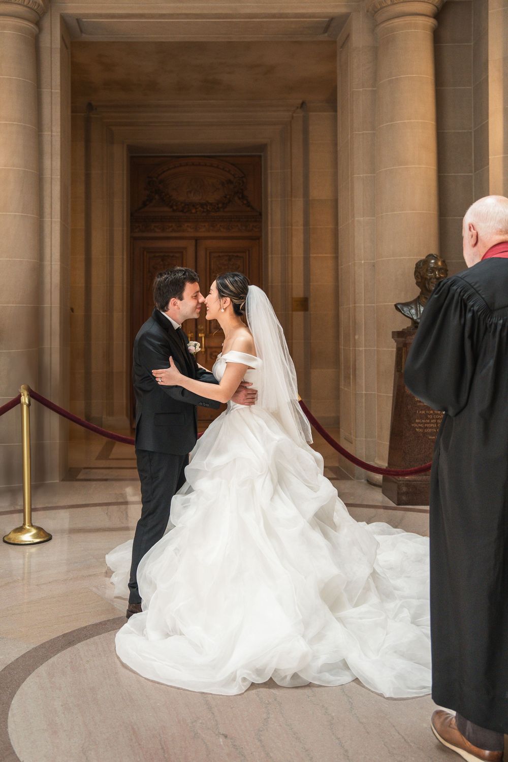 Wedding couple embraces in front of exquisite marble columns and architectural details at city hall.