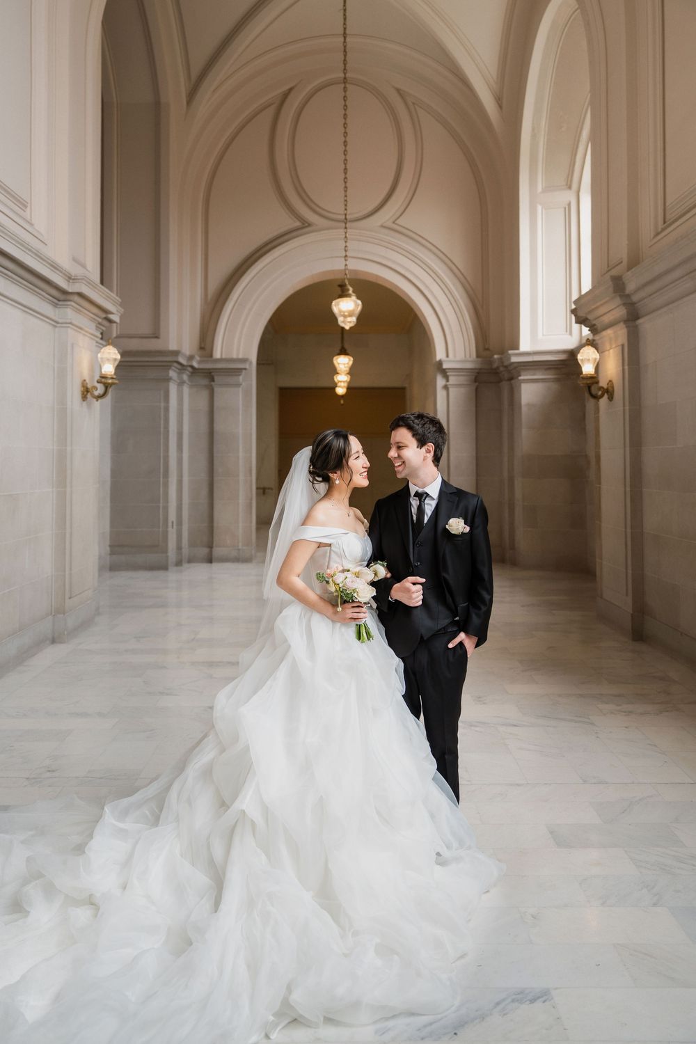 Elegant wedding portraits in a classic white marble corridor with arched ceilings and warm lighting.