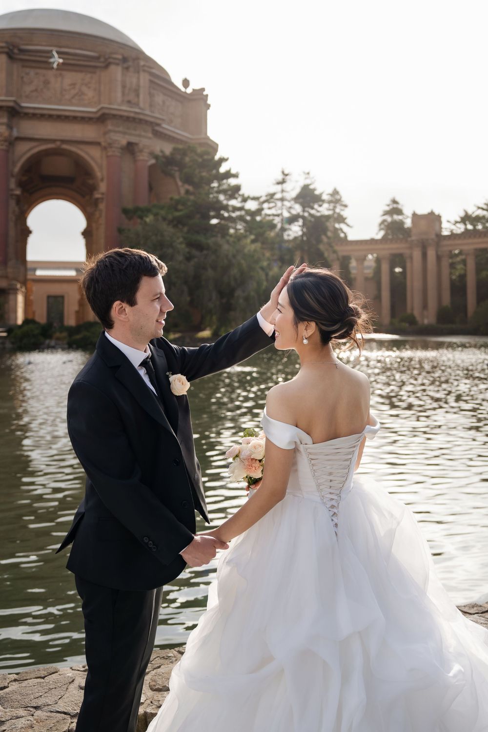 A romantic wedding photoshoot at the Palace of Fine Arts in San Francisco with a couple in formal attire by the lagoon.