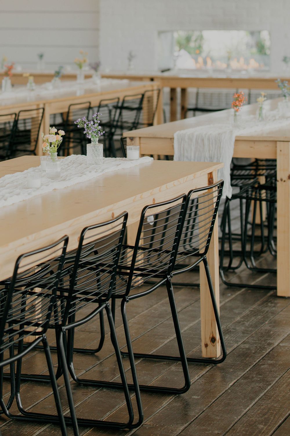 Long wooden tables with black metal chairs arranged for a wedding reception.