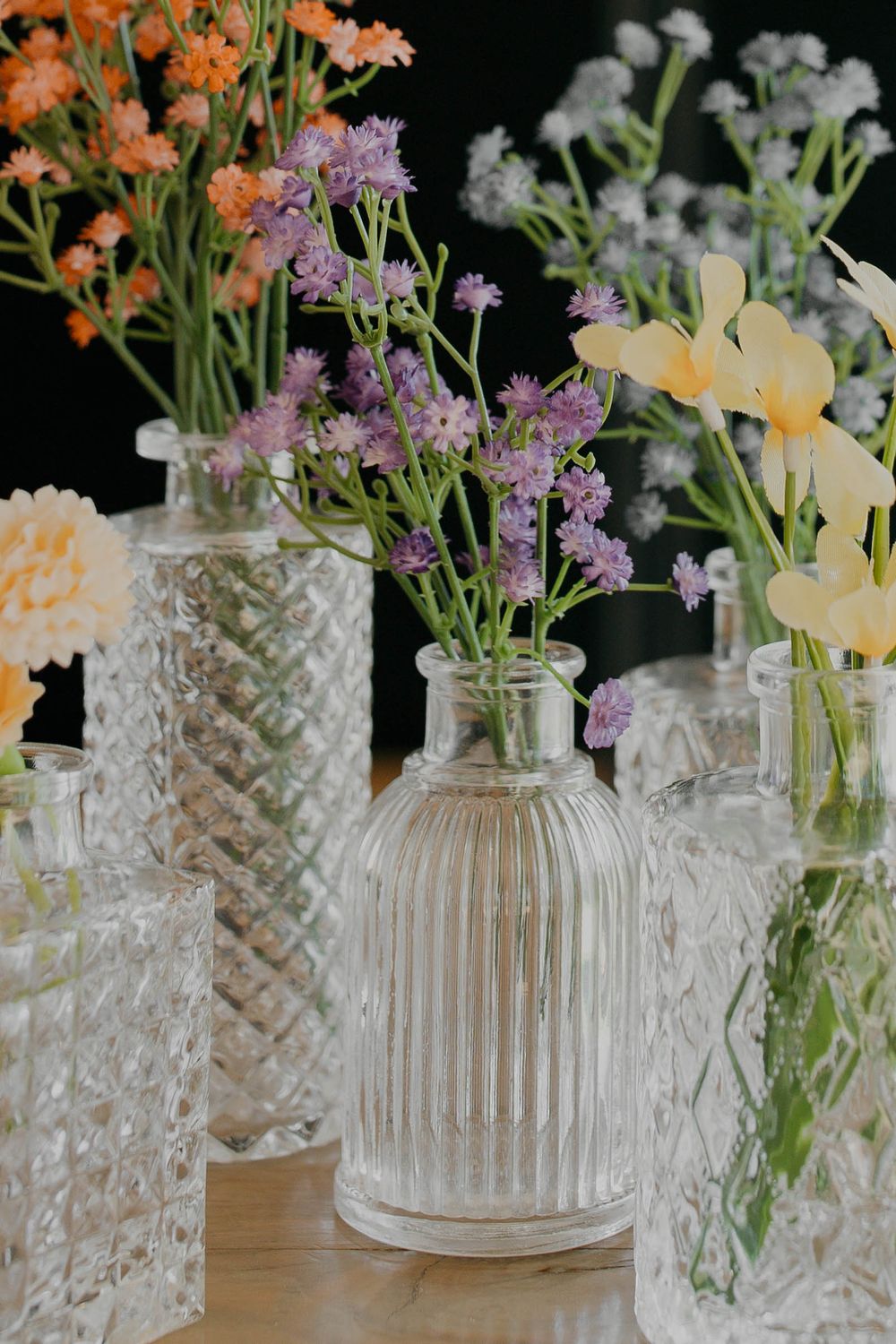 Delicate spring flowers in orange and purple arranged in vintage glass vases on a lace tablecloth.