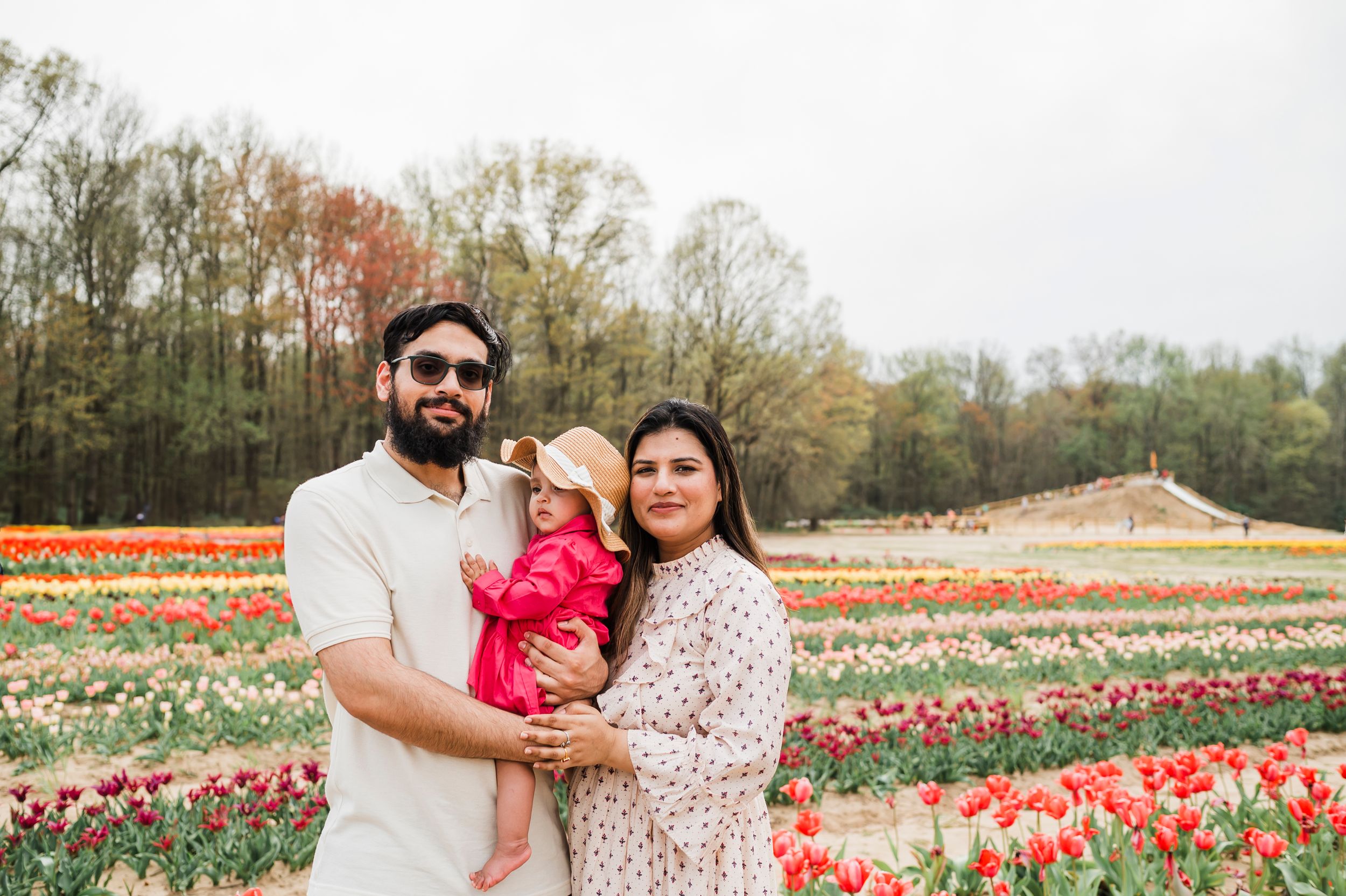 A couple and their child stand in a vibrant tulip field during springtime with blooming flowers in background.