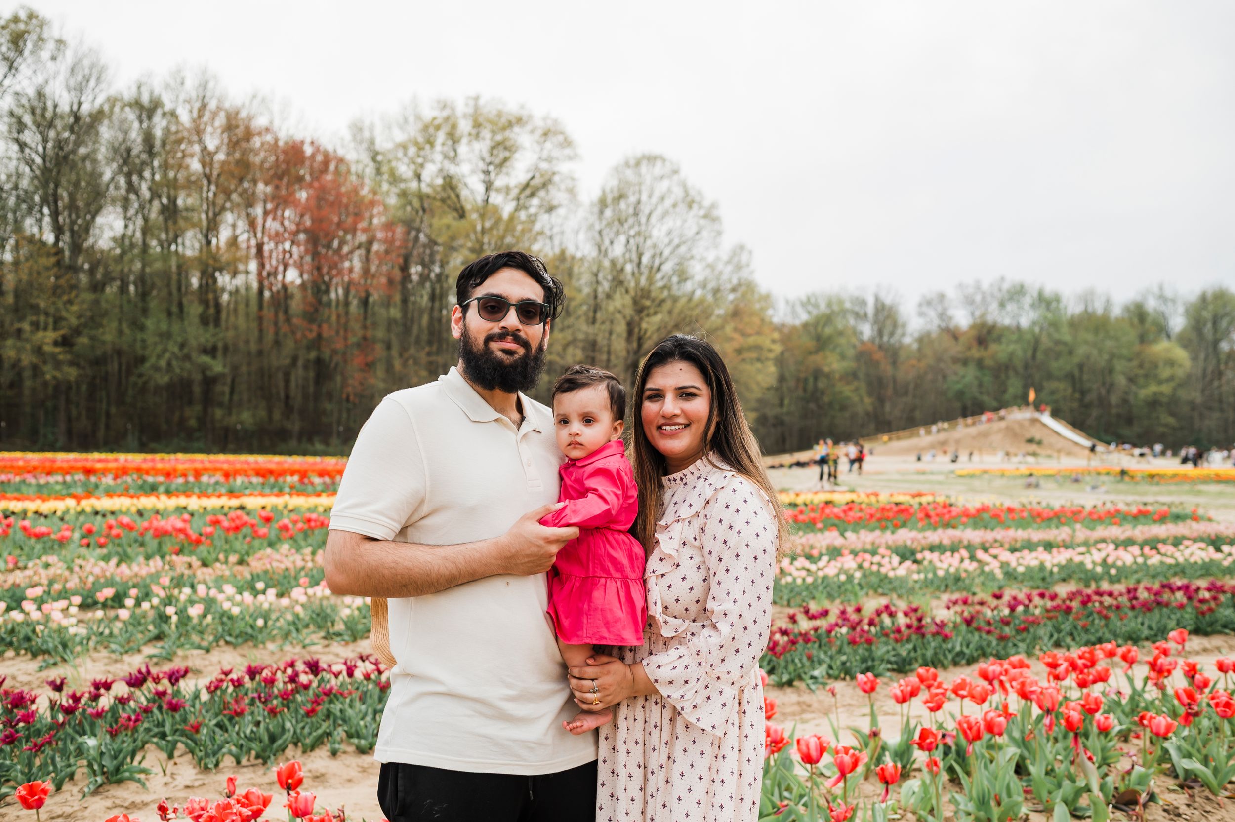A family stands together in a colorful tulip field with trees in the background on an overcast spring day.