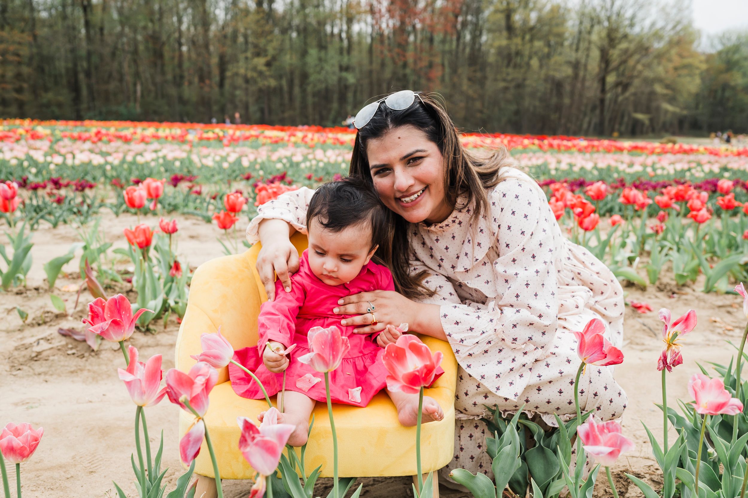 Two people in spring clothing smile together among vibrant pink and red tulips in a blooming garden field.