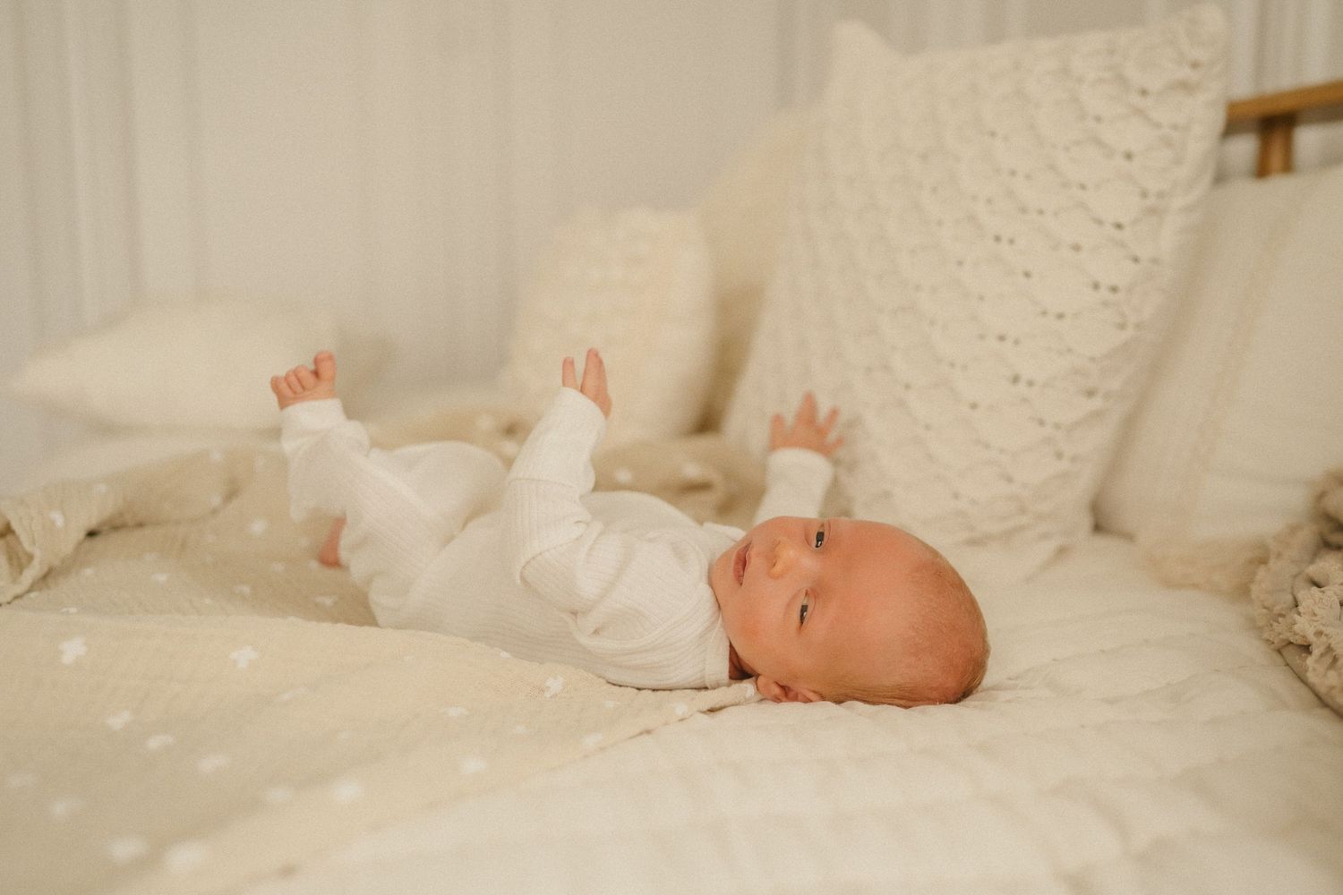 Baby in white linen blankets lies on soft textured bedding showing different gentle poses.