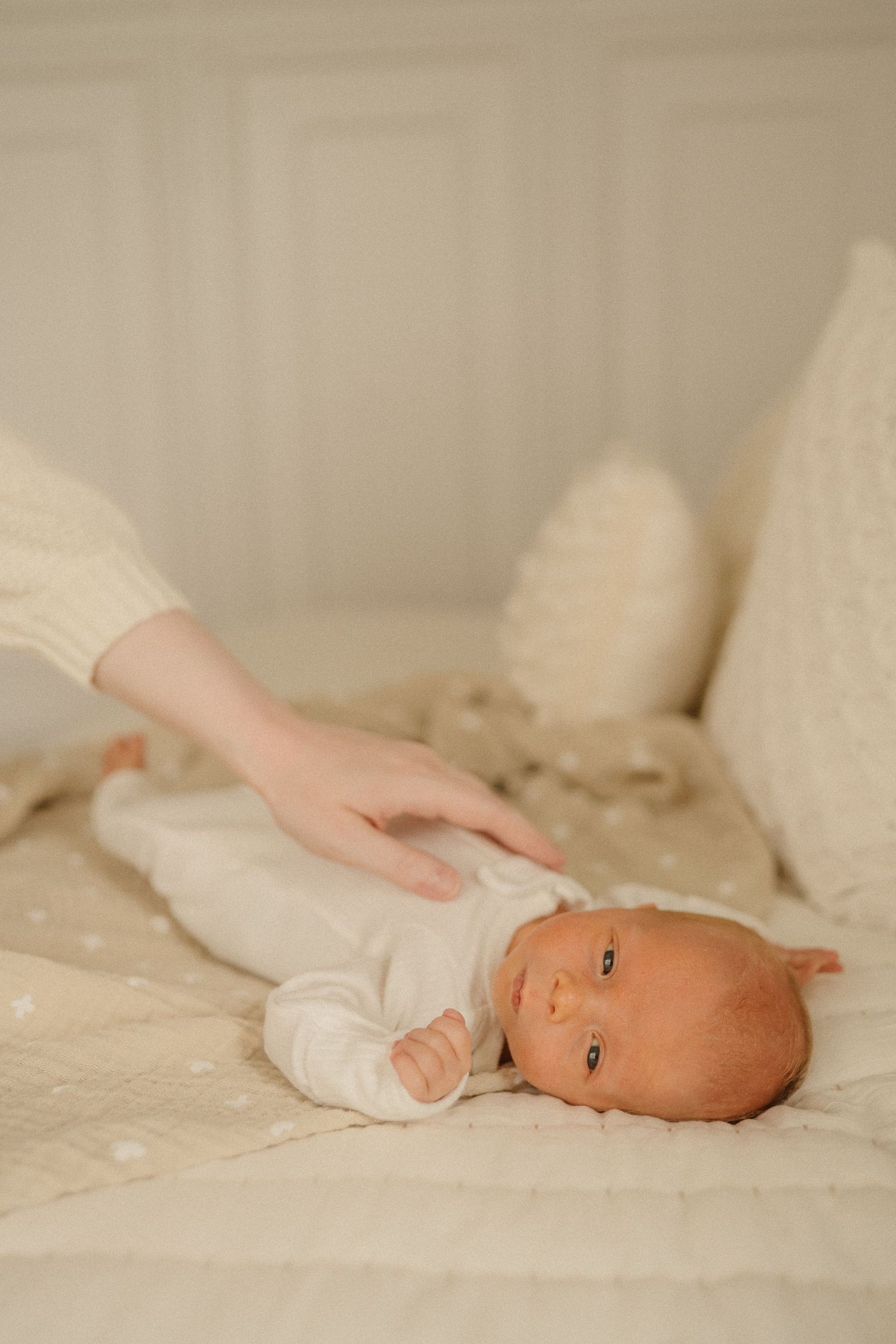 Peaceful newborn baby resting on cream colored textured blankets in soft lighting.