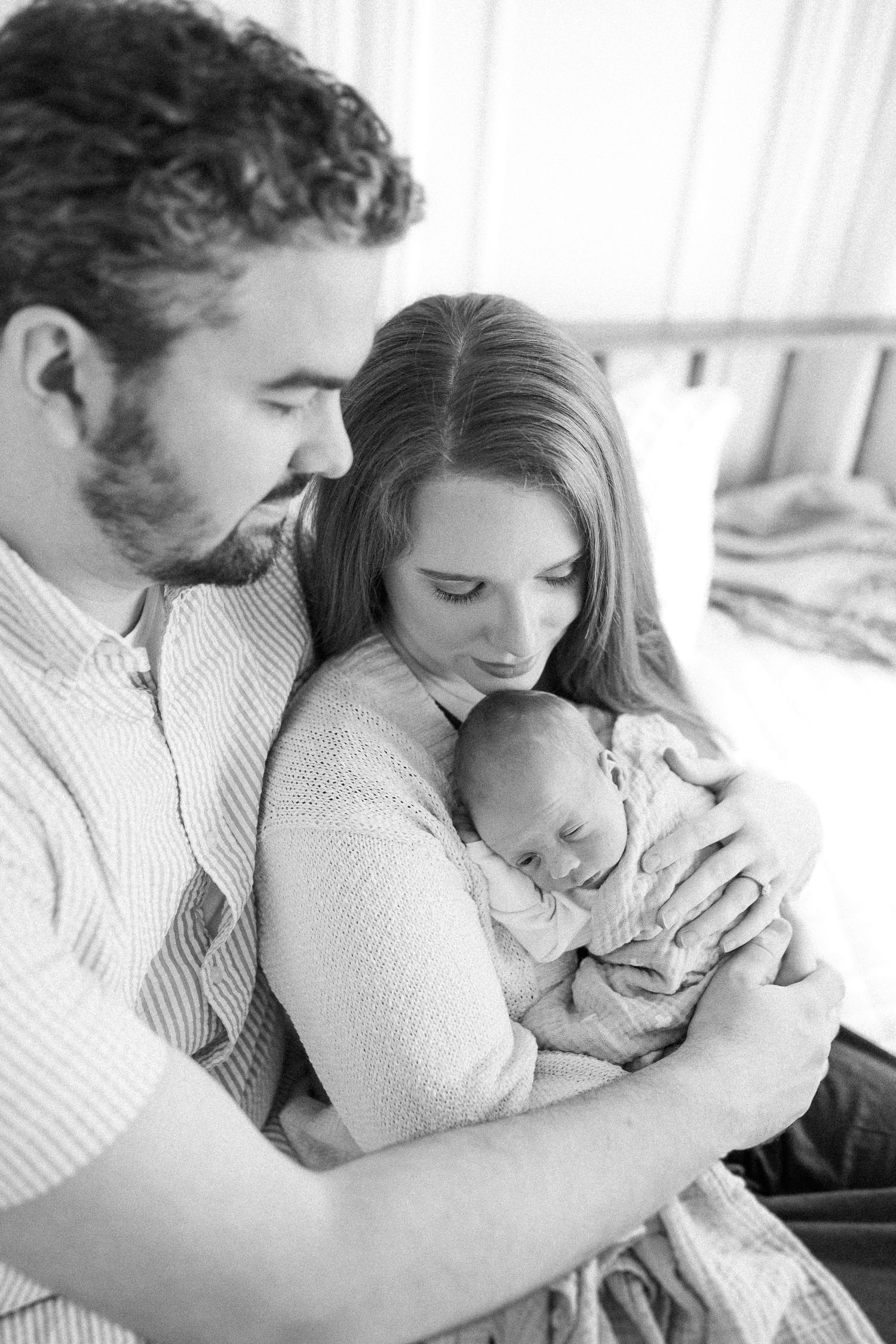 A tender black and white portrait of new parents cradling their sleeping newborn baby.