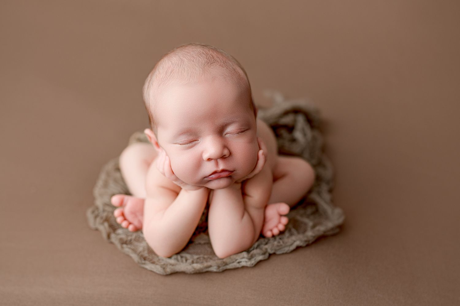 Sleeping newborn nestled in curved rattan bassinet with red knit blanket on white textured surface.