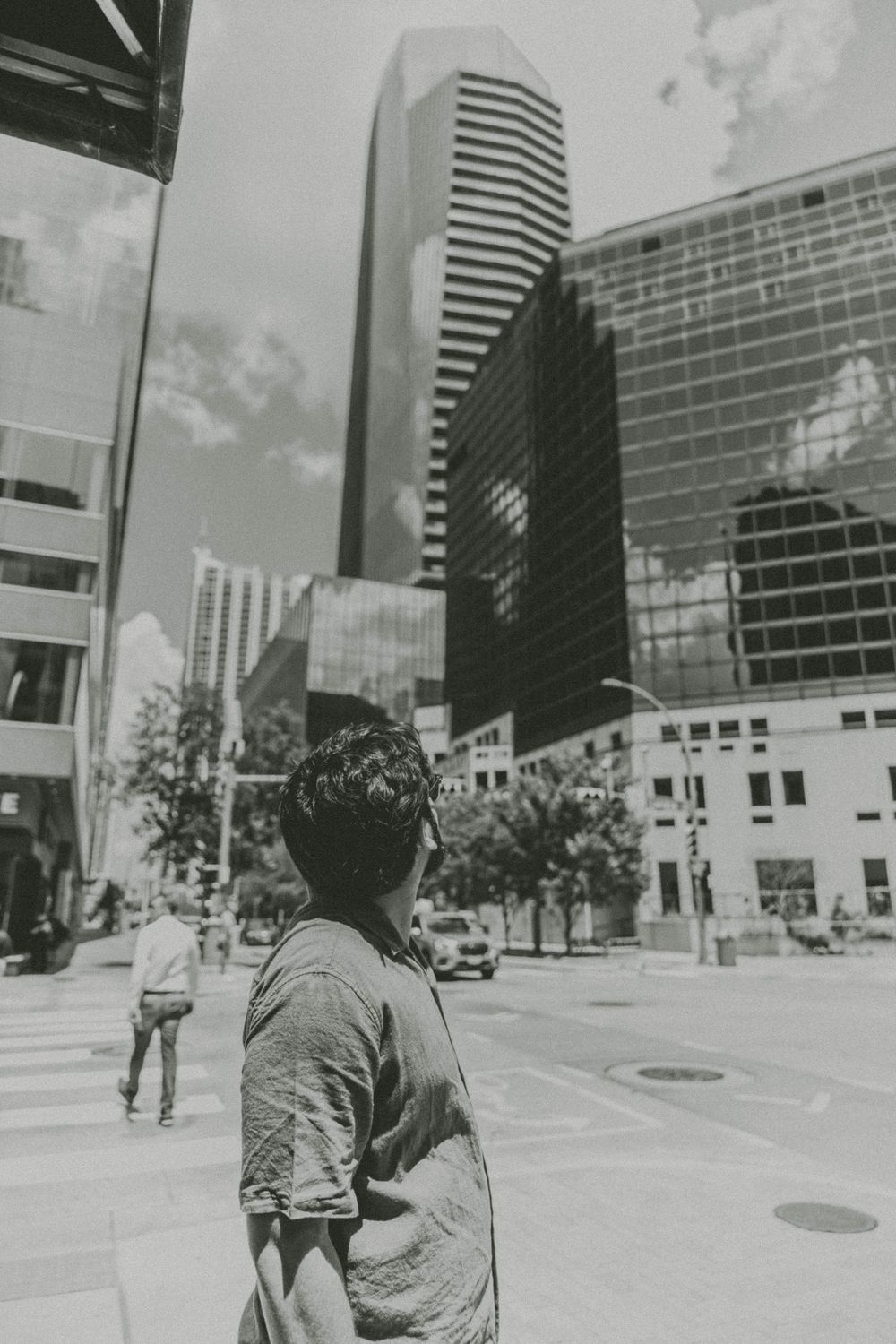 A person walking past modern office buildings in an urban setting, shown in three sequential black and white frames.