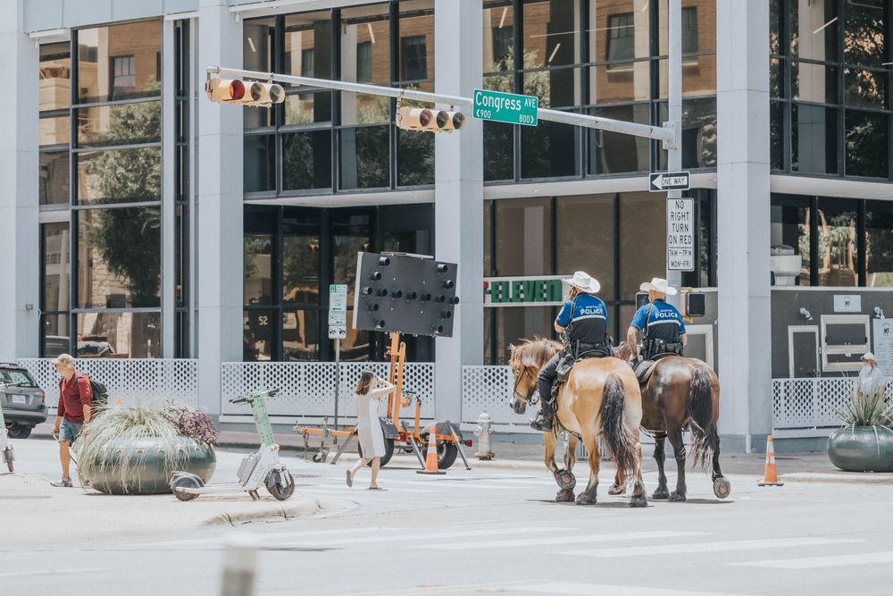 Modern city street scene with glass buildings and pedestrians walking in an open plaza area.