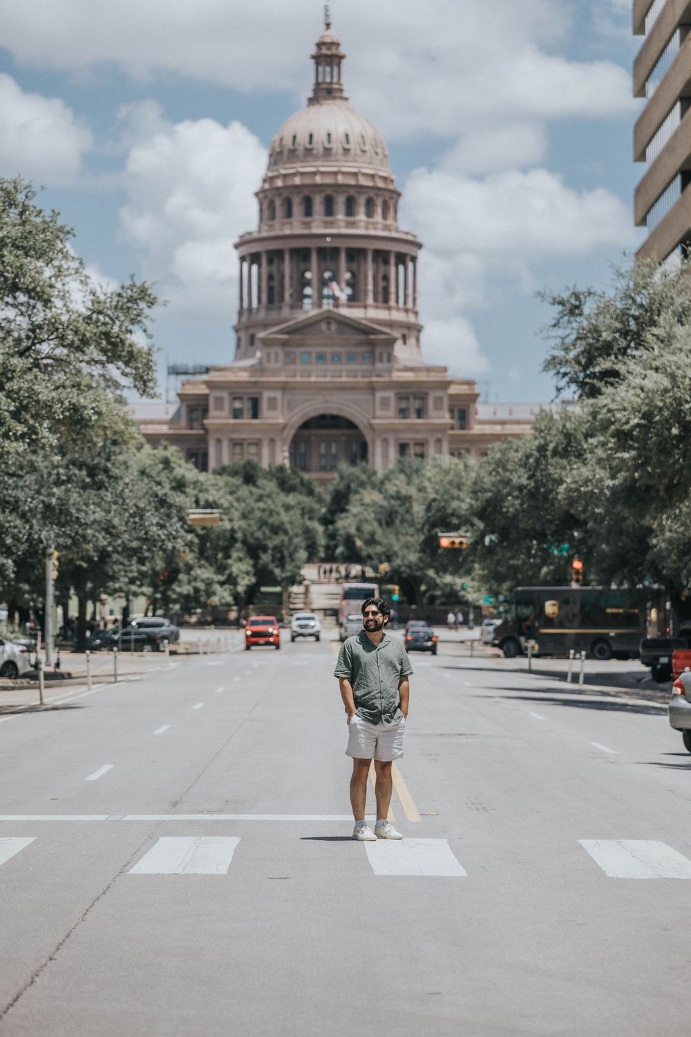 The Texas State Capitol building shown from a distance with a wide street and trees in the foreground.
