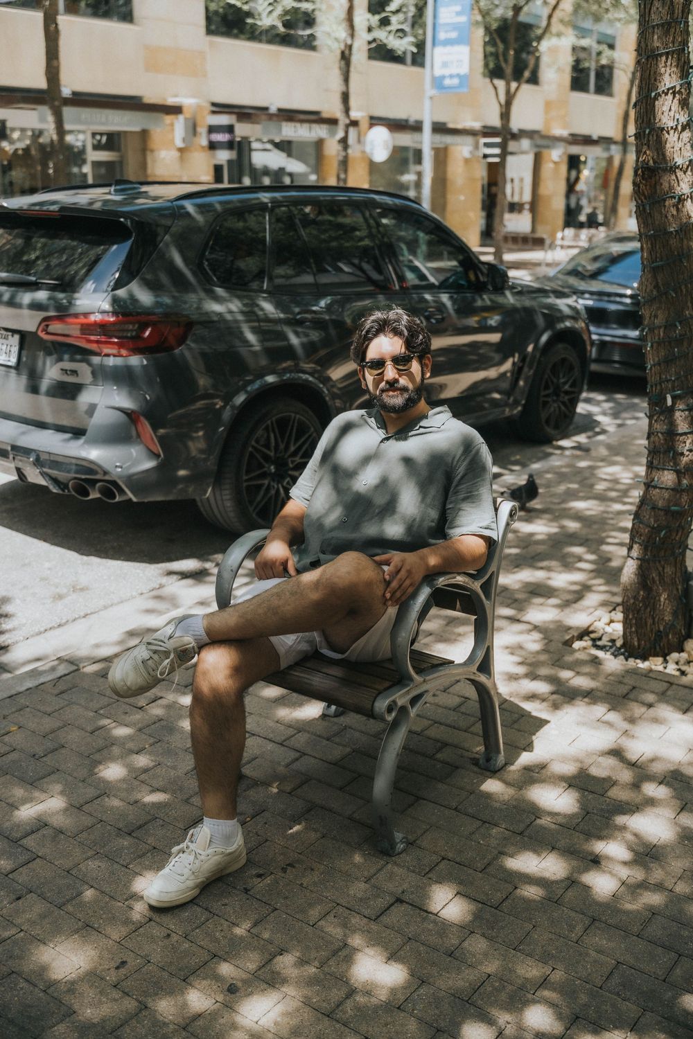 Person relaxing on a bench in a shaded urban area with parked cars visible in the background.