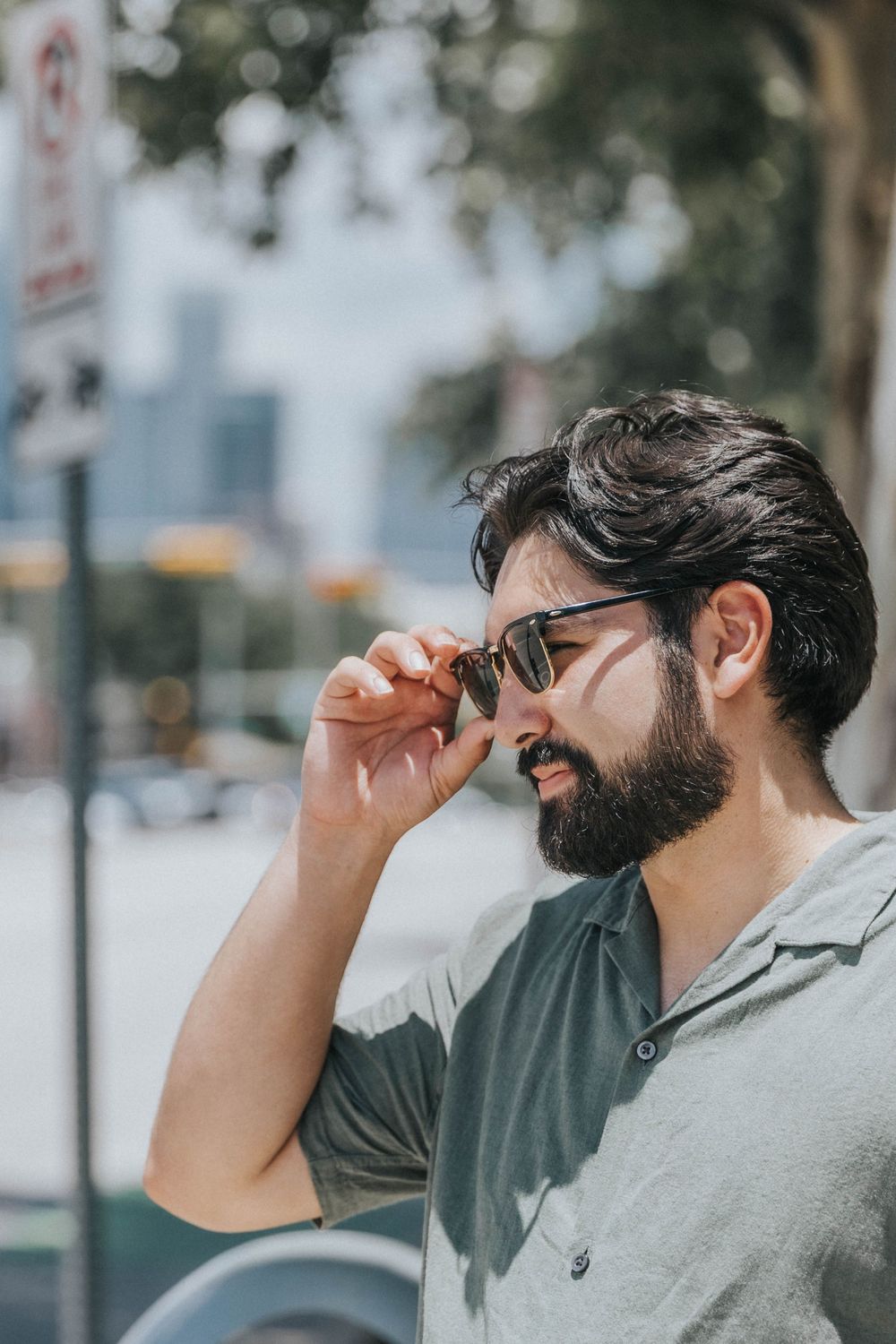 Stylish person with a beard and sunglasses enjoys a moment in an urban setting.