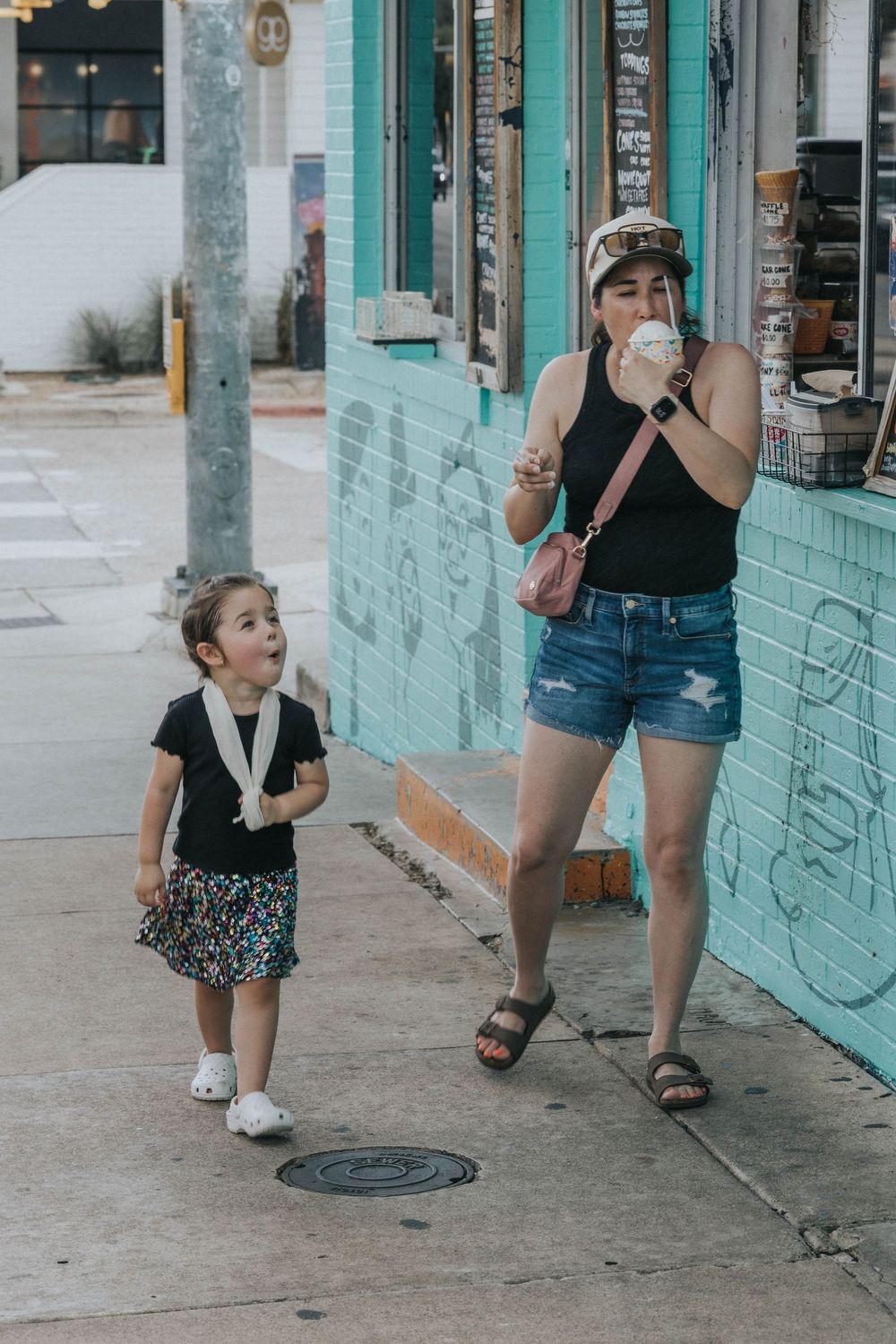 Two people enjoying ice cream treats on a sidewalk next to a turquoise-colored building on a sunny day.