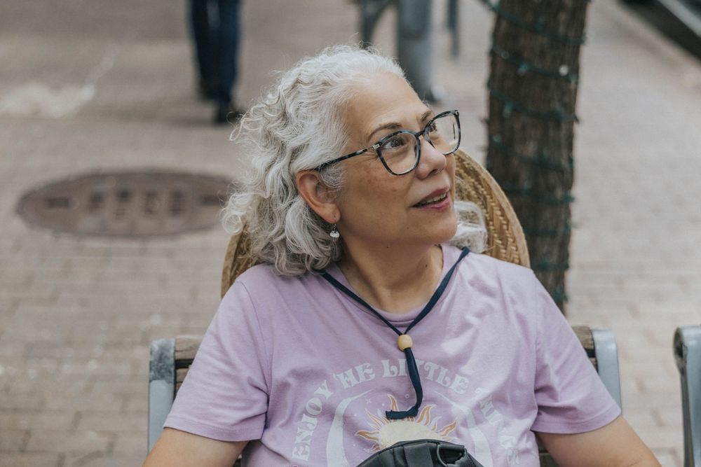 Contemplative person in glasses wearing a casual purple t-shirt relaxes outdoors on a sunny day.