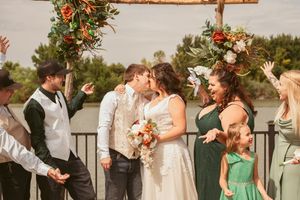 Wedding celebration captured in warm light with attendees showing joyful reactions under floral-decorated wooden arch.