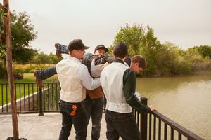 Groomsmen share a fun group moment on a waterfront deck during a wedding celebration.