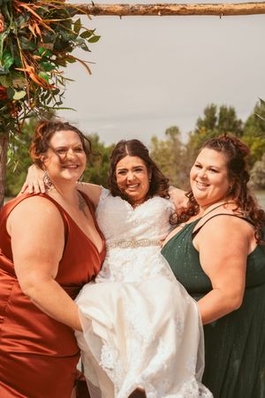 A joyful group moment captured at an outdoor wedding with people embracing in rust and forest green attire.