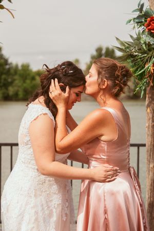 Two people in wedding attire share an intimate moment on a deck during an outdoor celebration.